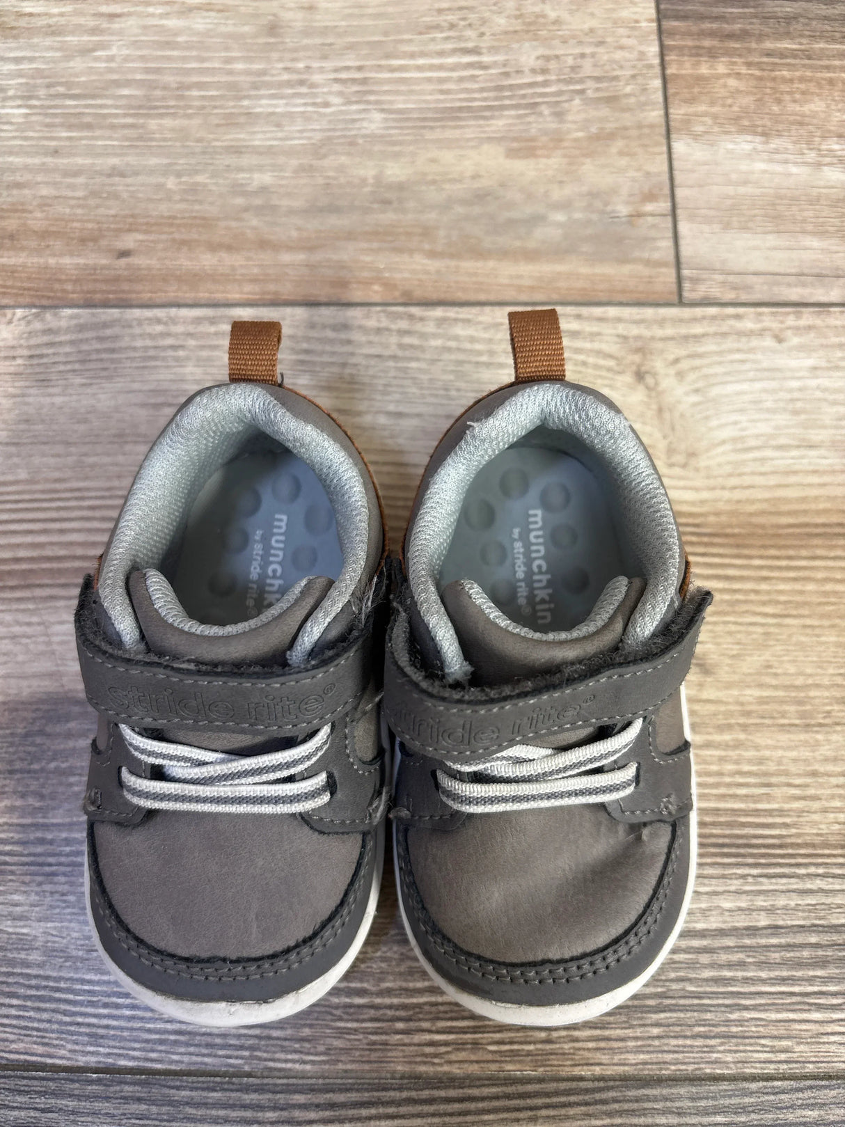 Top view of toddler Munchkin by Stride Rite Miller grey sneakers showing velcro straps and elastic laces on wood floor background