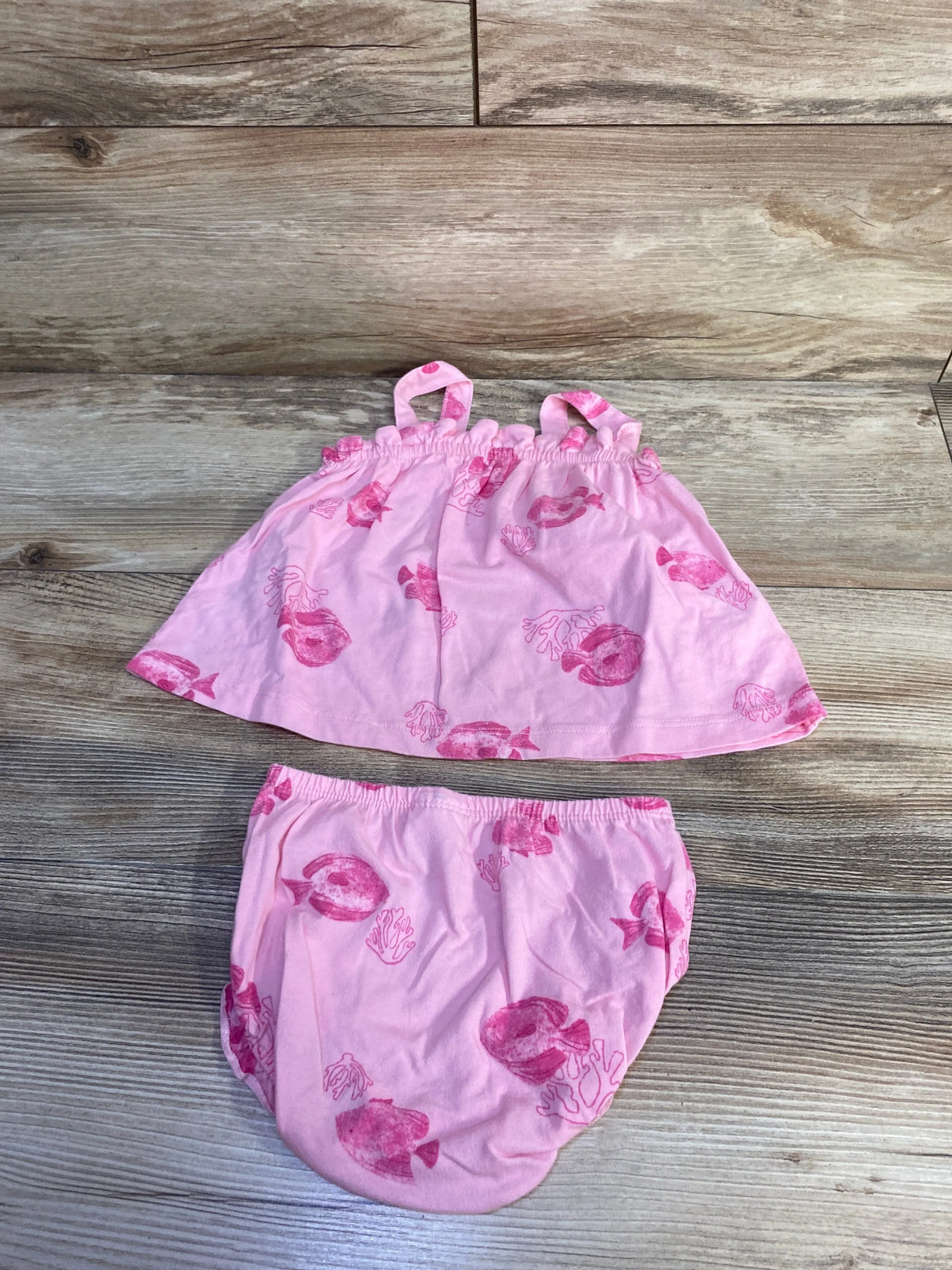 Top down view of pink tank top and bloomer set showcasing fish print and elastic waist and straps on wood background