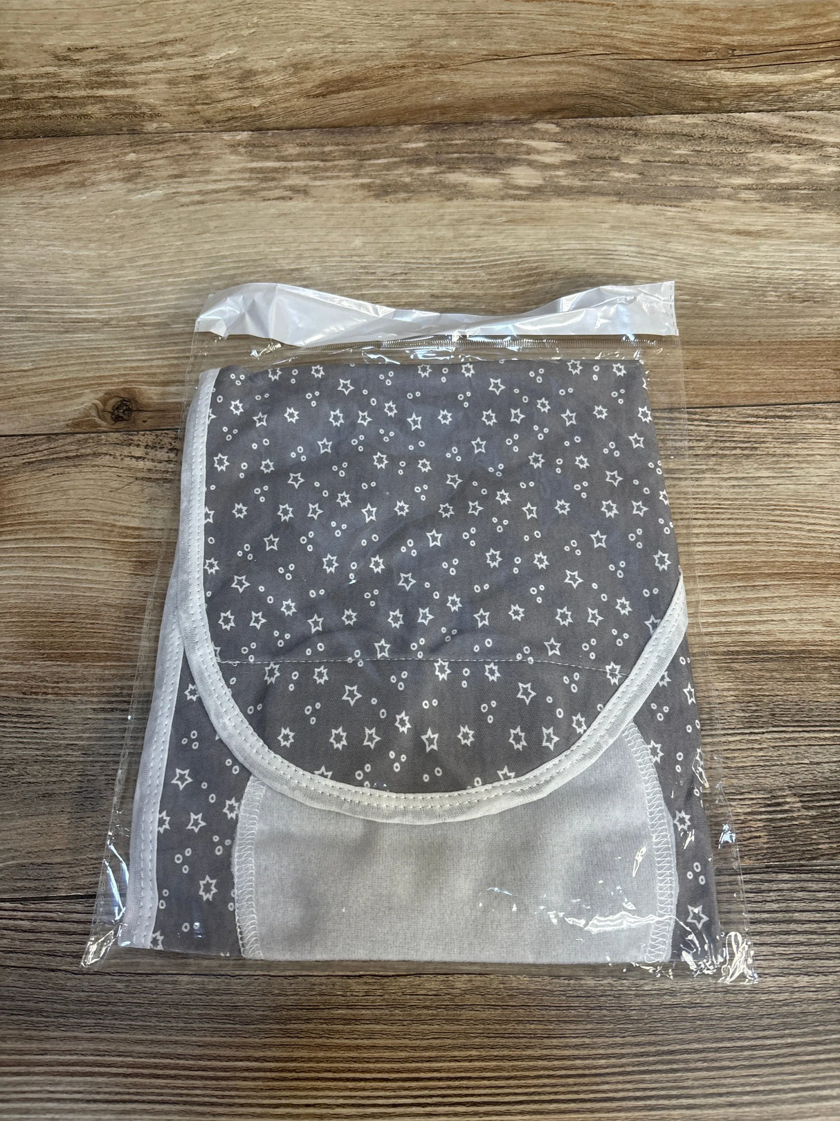 Folded flat view of NEW Ramede swaddle wrap with hat size 0-3m showcasing grey fabric with white star print and white trim on wood surface