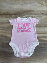 Flat lay of pink UNLV Love Rebels baby bodysuit showing ruffled cap sleeves and three snap closures on wood background