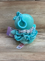 Plush teal baby toy with clip, ruffled dress, and bow, on wood background