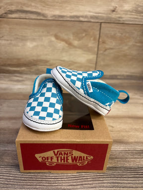 Front and side view of baby Vans Slip-On crib shoes showing blue-and-white checkerboard pattern on a Vans box on wood floor