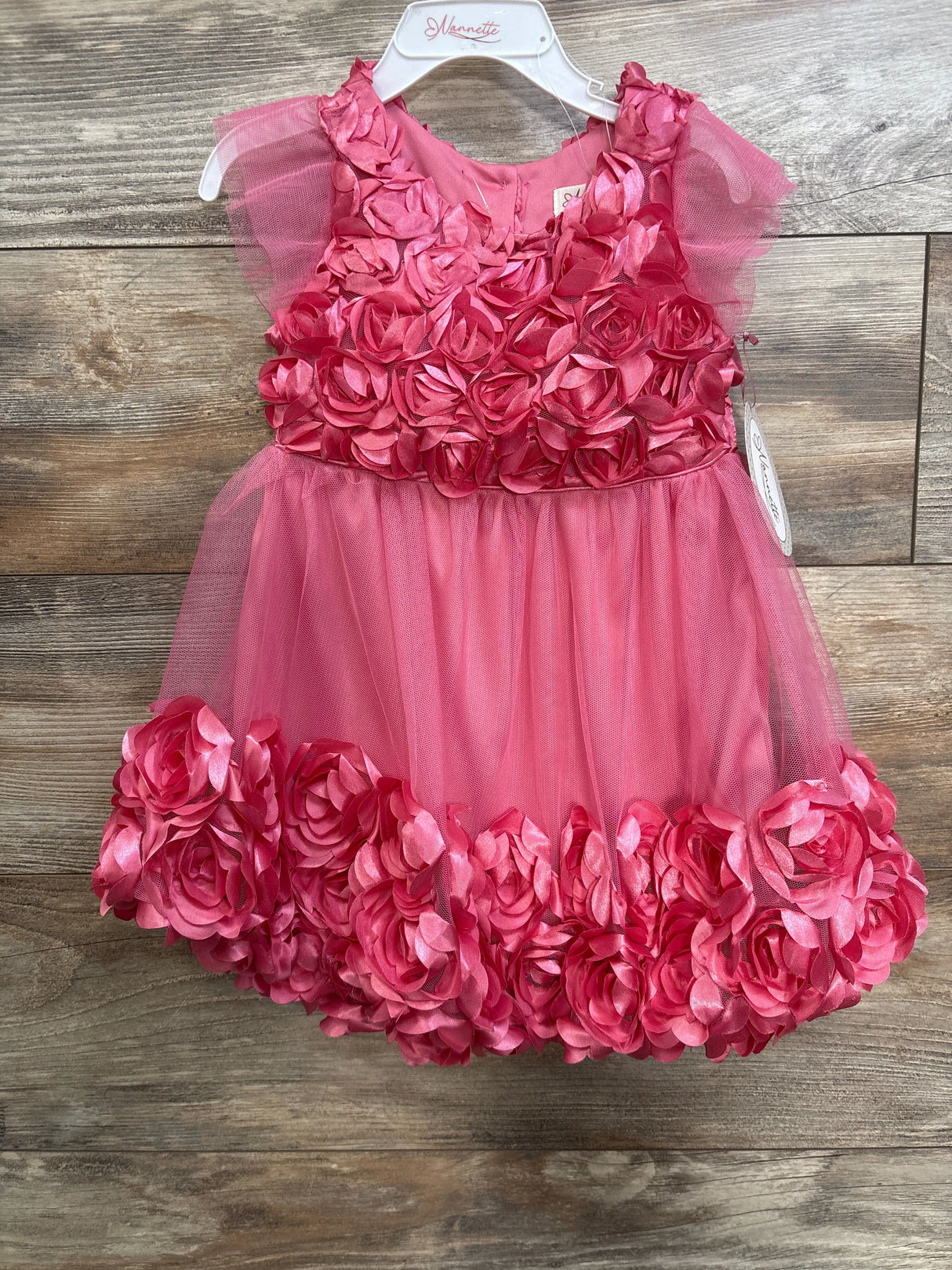 Front view of pink rosette dress size 3T showcasing satin rose appliqués on bodice and hem with tulle skirt on wood floor