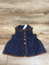 Front view of navy quilted peplum vest showcasing brown trim, rounded collar, gold buttons, and flared hem on wood grain
