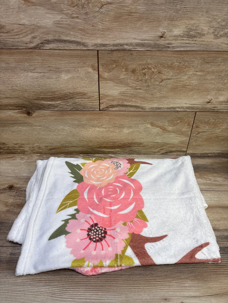 Folded white milestone blanket showcasing a colorful floral print on a wood floor