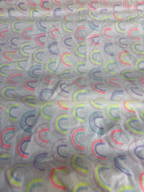 Top-down view of Cloud Island fitted crib sheet showcasing repeating pastel rainbow arc print on white background