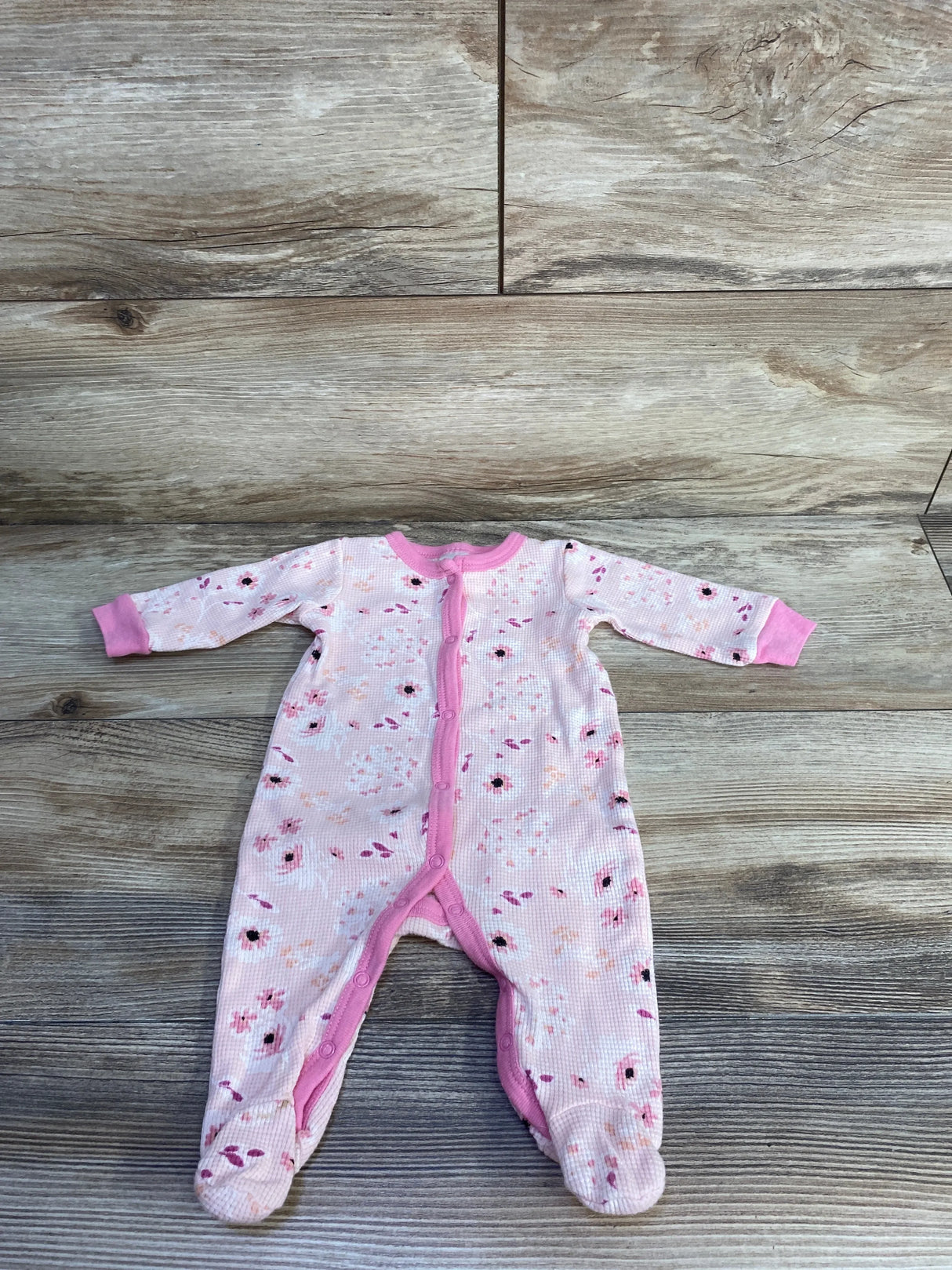 Flat lay of pink waffle-knit footed sleeper (3-6 months) showing front snap closure and floral print on wood background