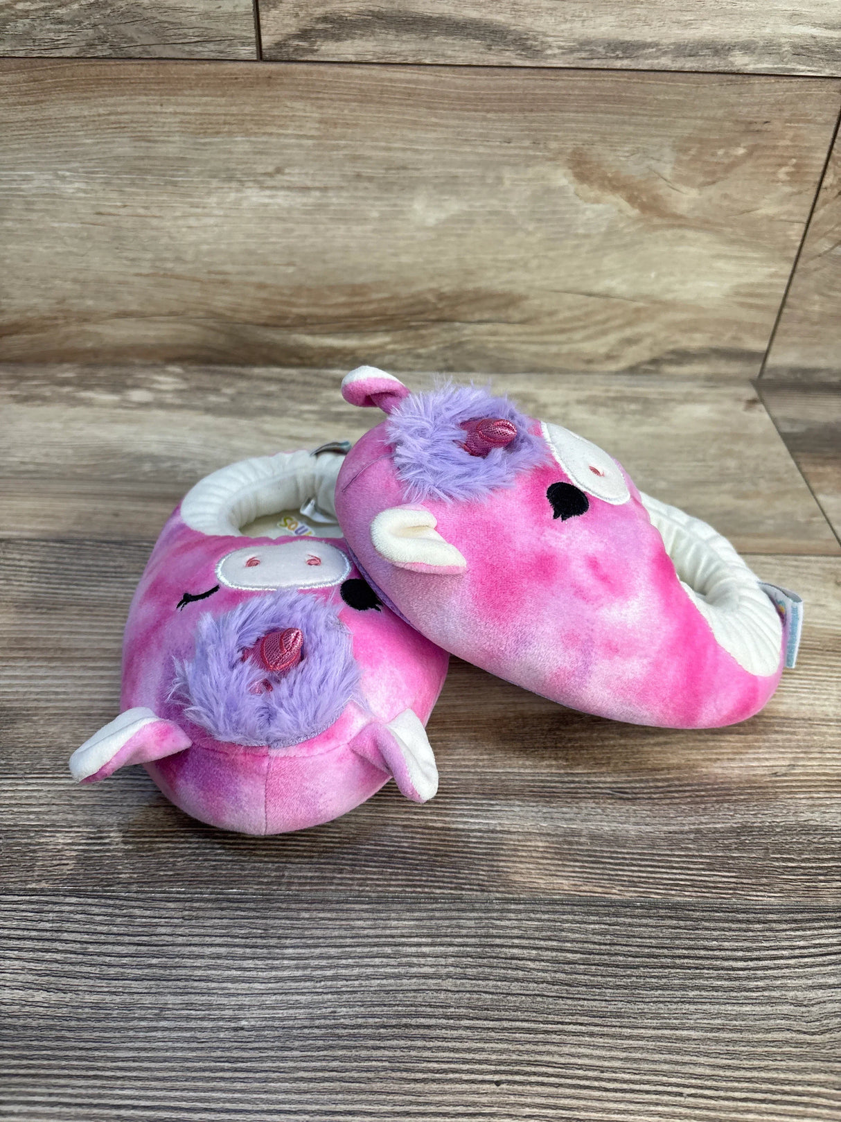 Pink unicorn plush baby slippers with purple accents on wood background