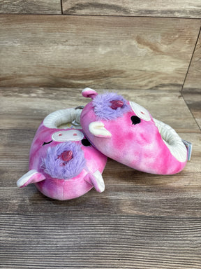 Pink unicorn plush baby slippers with purple accents on wood background