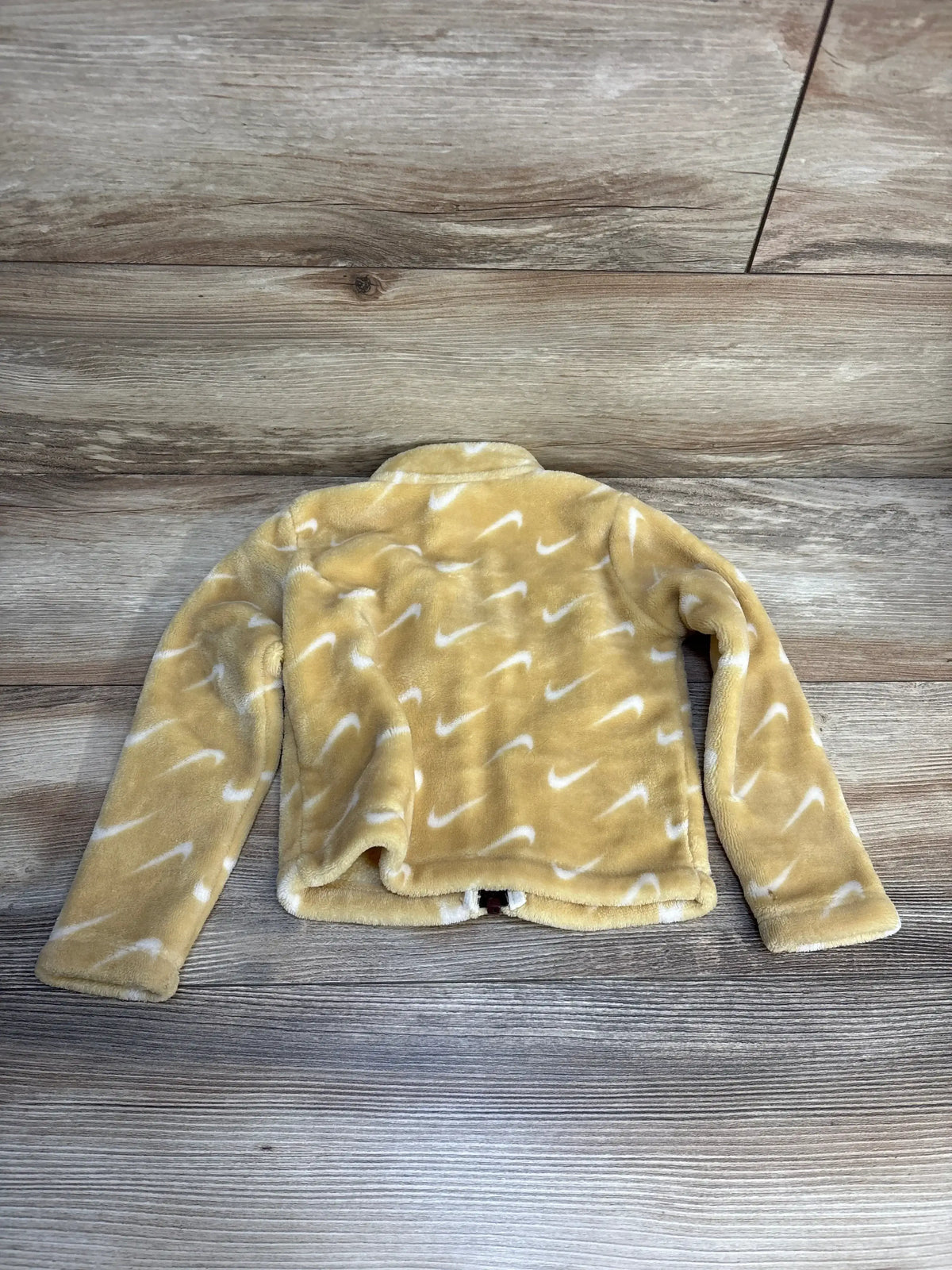 Soft yellow kids fleece jacket with white swoosh pattern, laid flat on wood floor