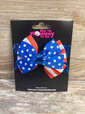Front view of American flag glitter hair bow showcasing blue star-patterned and red-and-white striped layered ribbons with glitter base on a black display card over a wood surface