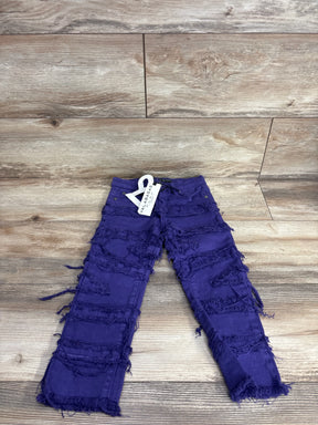 Purple distressed kids jeans with frayed details on wood floor background