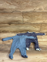 Flat lay of Cloud Island 2-pack newborn sleeper set (0-3M) showing front zipper, footed legs, blue solid and navy bear-print sleepers on wood floor background