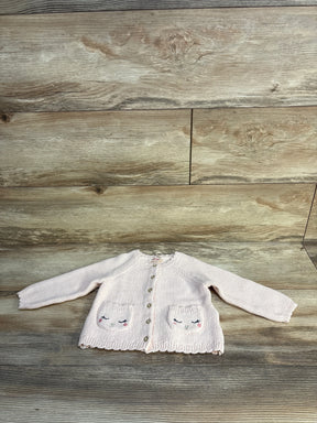 Light pink knit baby cardigan with embroidered faces on pockets, laid on wood floor
