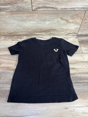 Black short sleeve kids t-shirt with a small gold logo on chest, laid on wood floor