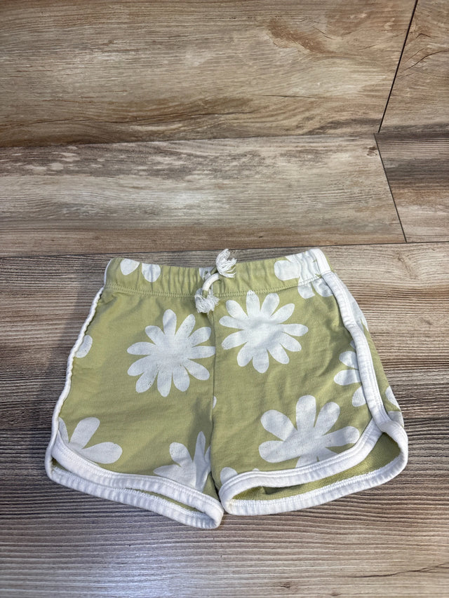 Green baby shorts with white daisy print, elastic waist, laid on wood floor