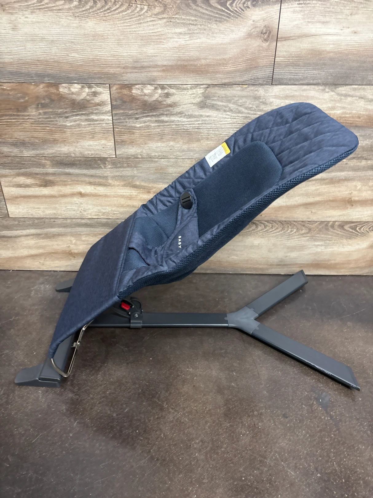 Navy blue baby bouncer seat with metal frame on wood and dark floor background