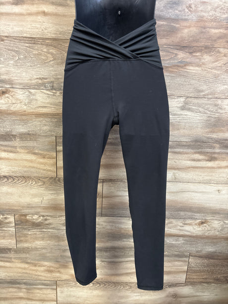 Front view of black maternity crossover panel leggings showcasing the crossed waistband with a wood plank background