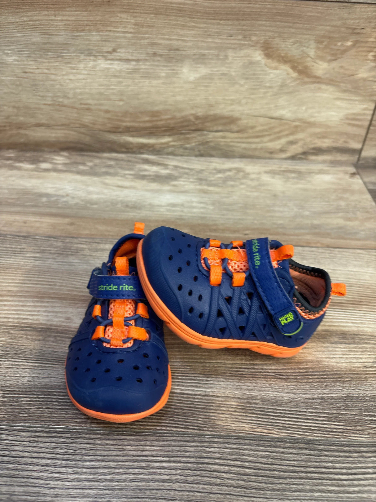Angled front view of Stride Rite Phibian toddler water shoes, navy with orange accents, perforated upper and elastic laces on wood background