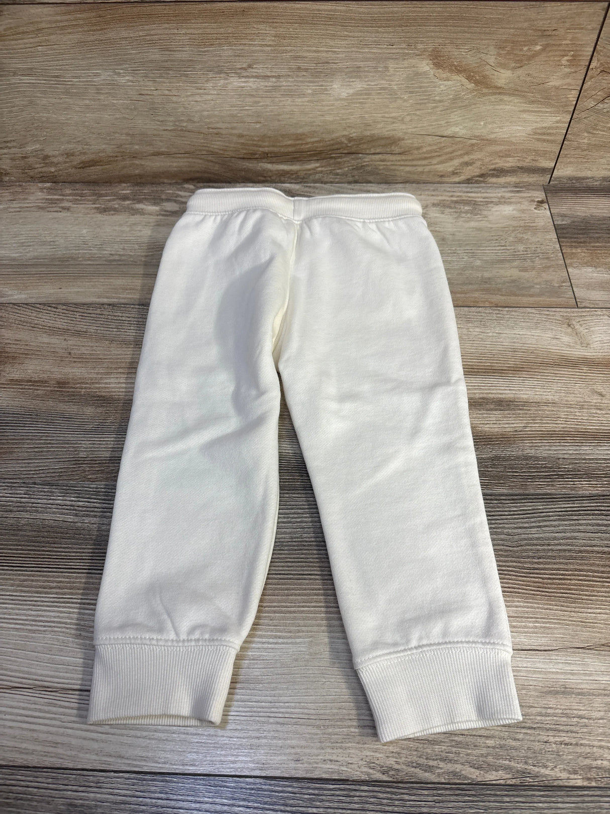 Back view of cream Oshkosh fleece toddler joggers showing elastic waistband and cuffed ankles on wood floor