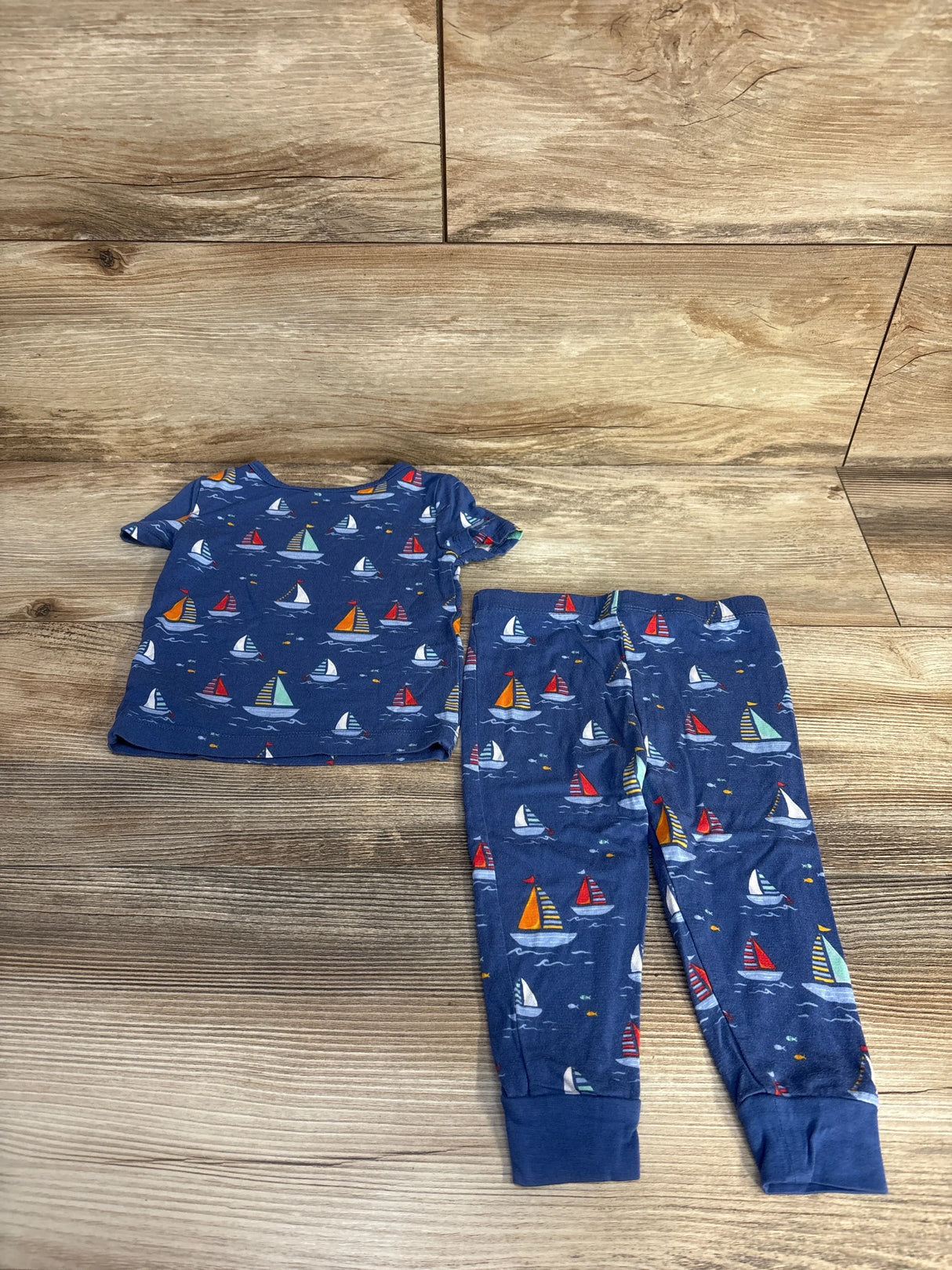 Front flat-lay of Little Me 2-piece bamboo pajama set in blue with sailboat print and cuffed pant ankles on wood backdrop
