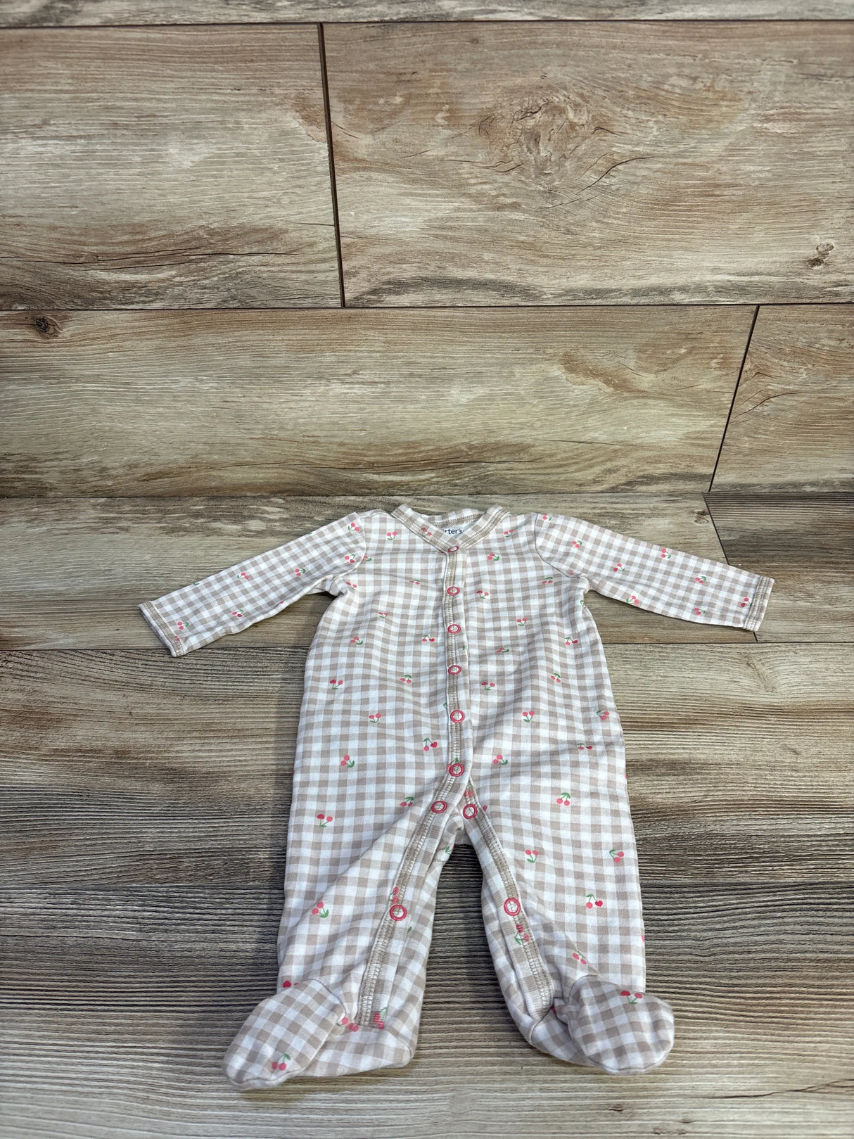 Flat lay of Carter's beige gingham baby sleeper with cherry print, front snap closure and built-in footies on wood background