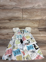 Vintage-style baby dress with sewing pattern print, ruffled sleeves, and scalloped hem on wood floor