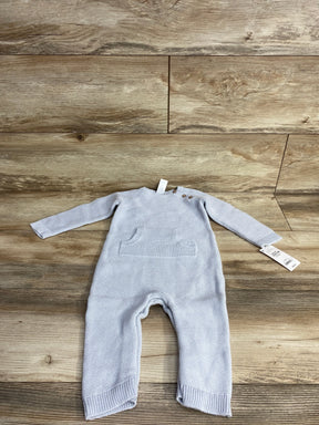 Light blue knitted baby romper with front pocket and wooden buttons on wood background