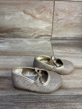 Angled side view of Koala Kids gold glitter bow ballet flats showing glitter finish, bow and elastic strap on wood background