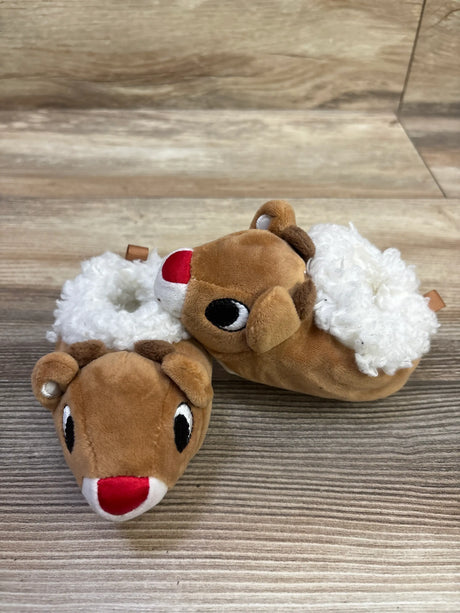Angled view of brown Rudolph the Red-Nosed Reindeer plush slippers with red noses, antlers, and white fluffy cuffs on a wood floor