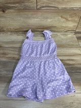 Flat lay of purple polka-dot shortie romper showing ruffled shoulder straps and smocked waist on light wood background