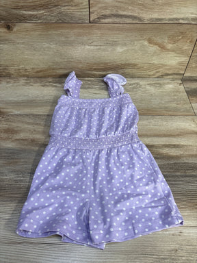 Flat lay of purple polka-dot shortie romper showing ruffled shoulder straps and smocked waist on light wood background