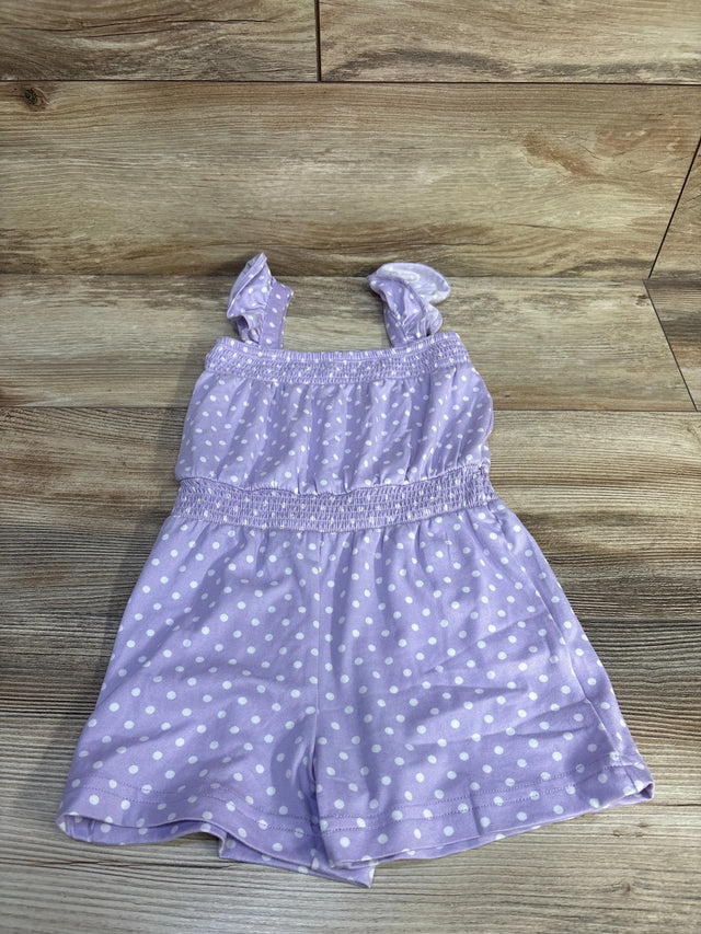 Flat lay of purple polka-dot shortie romper showing ruffled shoulder straps and smocked waist on light wood background