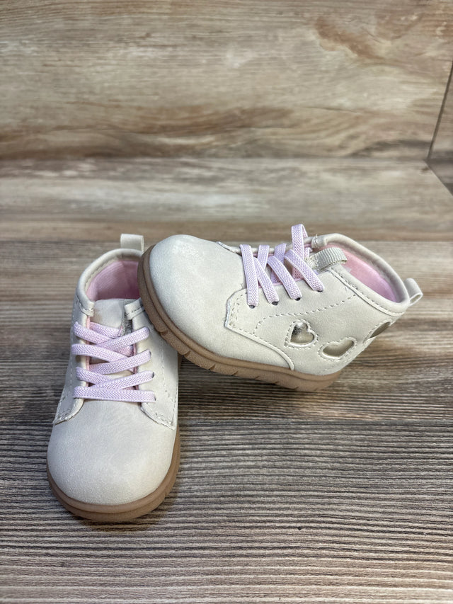 Light pink toddler shoes with heart cutouts and laces on wooden surface