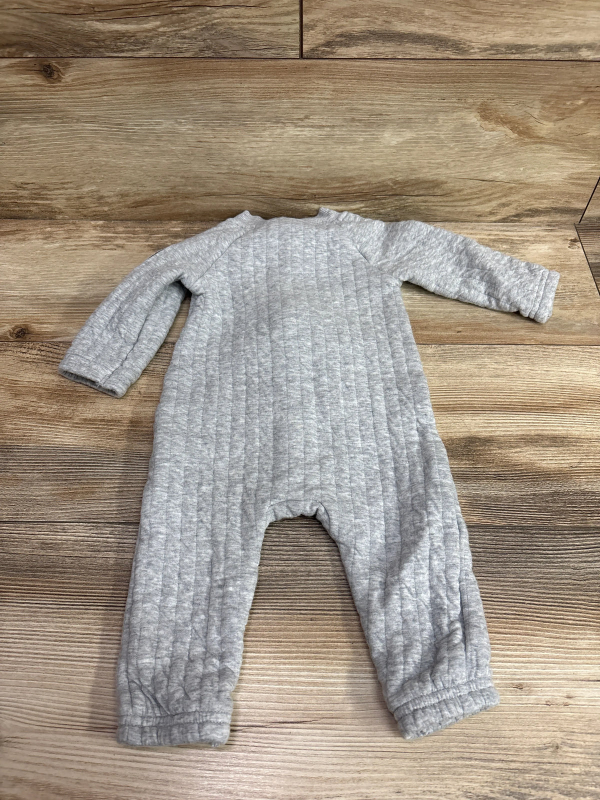 Top view of Carters gray quilted coverall in size 6 months showing long sleeves and ribbed cuffs on a wood surface