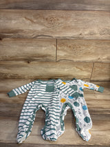 Top-down view of two newborn footed coveralls (2-pack) showcasing a green-striped coverall with chest pocket and a space-print coverall on wood background