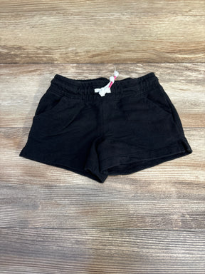 Flat-lay of black knit toddler shorts with elastic waistband, white drawstring, and front pockets on wood background
