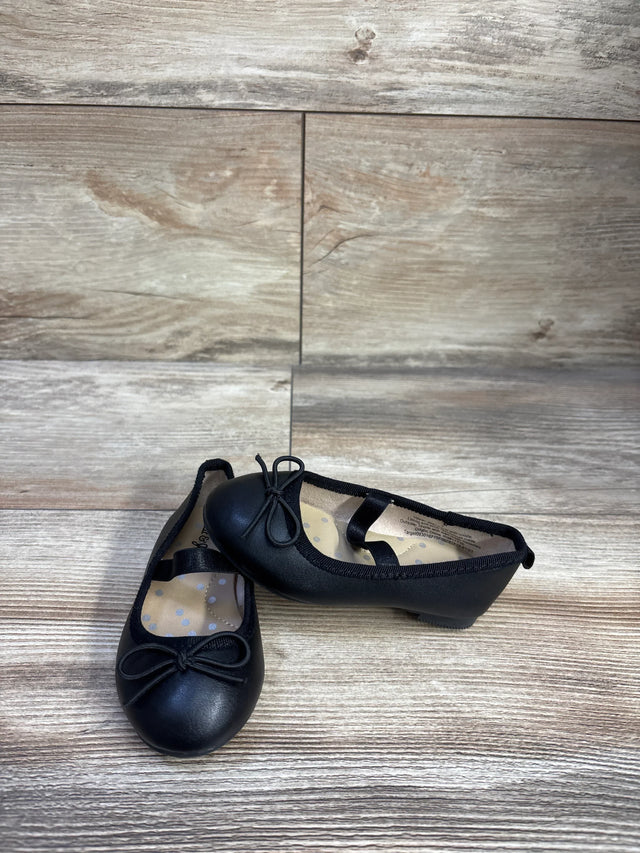 Angled front view of Cat and Jack Nora toddler black slip-on ballet flats showing bow and elastic strap on wood background