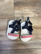 Top-down view of Child of Mine patriotic infant sandals showing navy crisscross ankle straps and red-and-white striped toe straps on wood floor