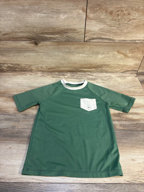 Green short sleeve kids shirt with white chest pocket on wood background