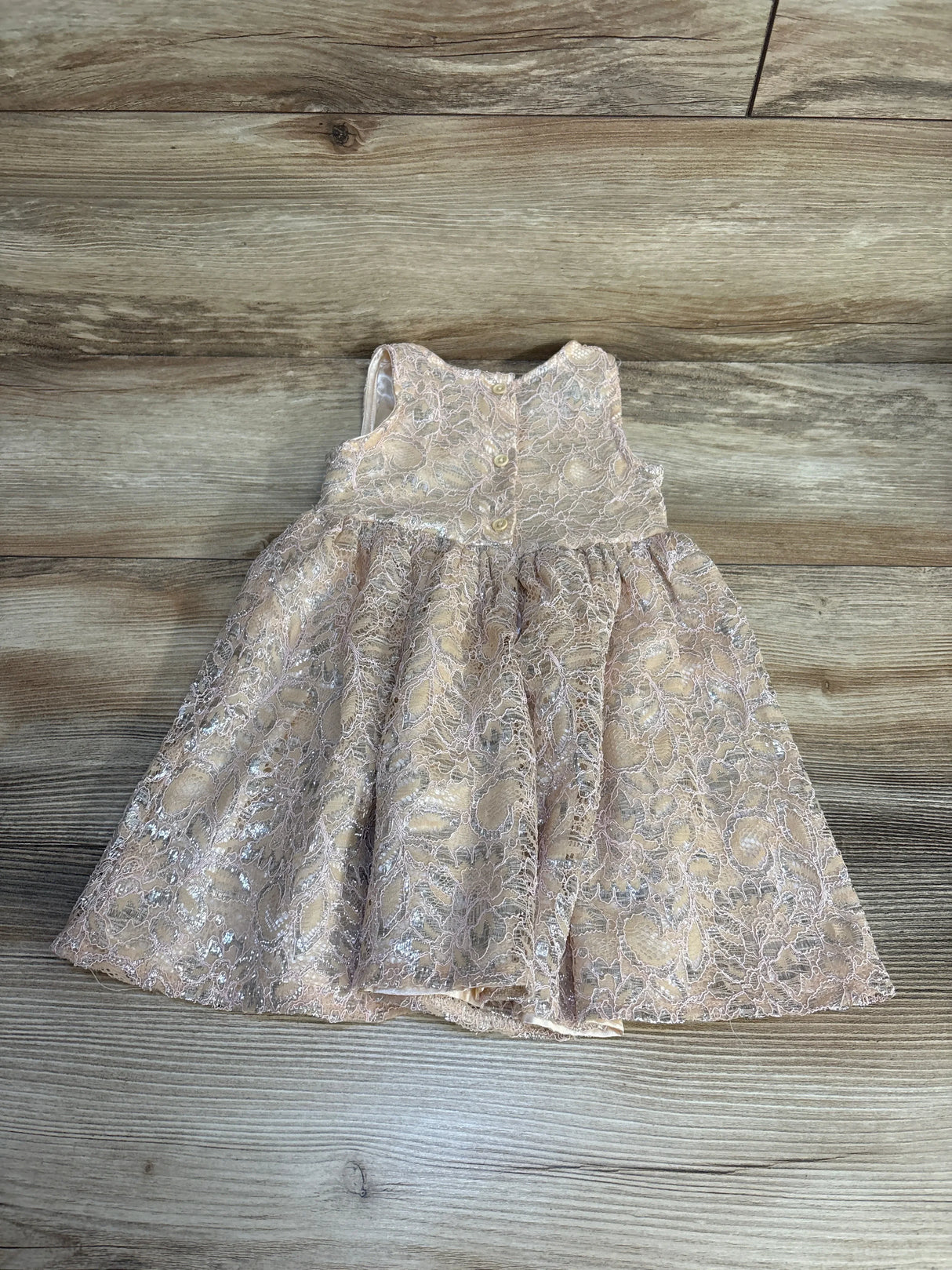Pink lace baby girl dress with floral pattern and buttons, displayed on wood background