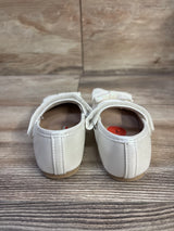 Rear view of Sugar Nira white baby flats showing back seam and hook-and-loop strap with glitter bow on wood-grain surface