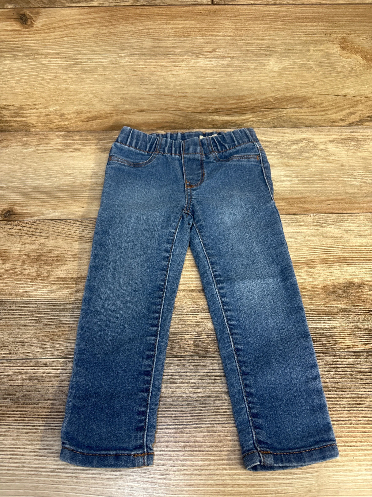 Blue denim jeans for kids with elastic waistband, displayed on wooden background