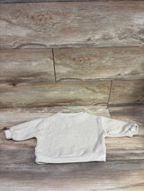 Back view of beige Snug Knit Initial E sweater showing ribbed knit texture and cuffs on wood flooring