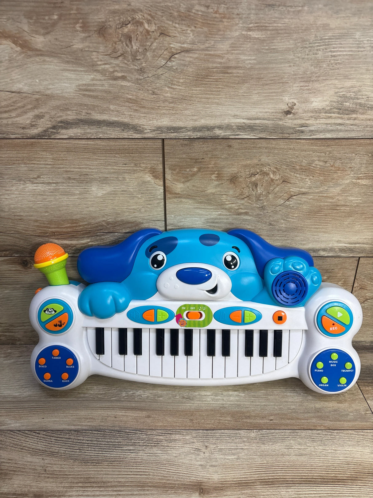Front view of Rolo's keyboard showing blue dog face, microphone, colorful buttons and piano keys on wood floor