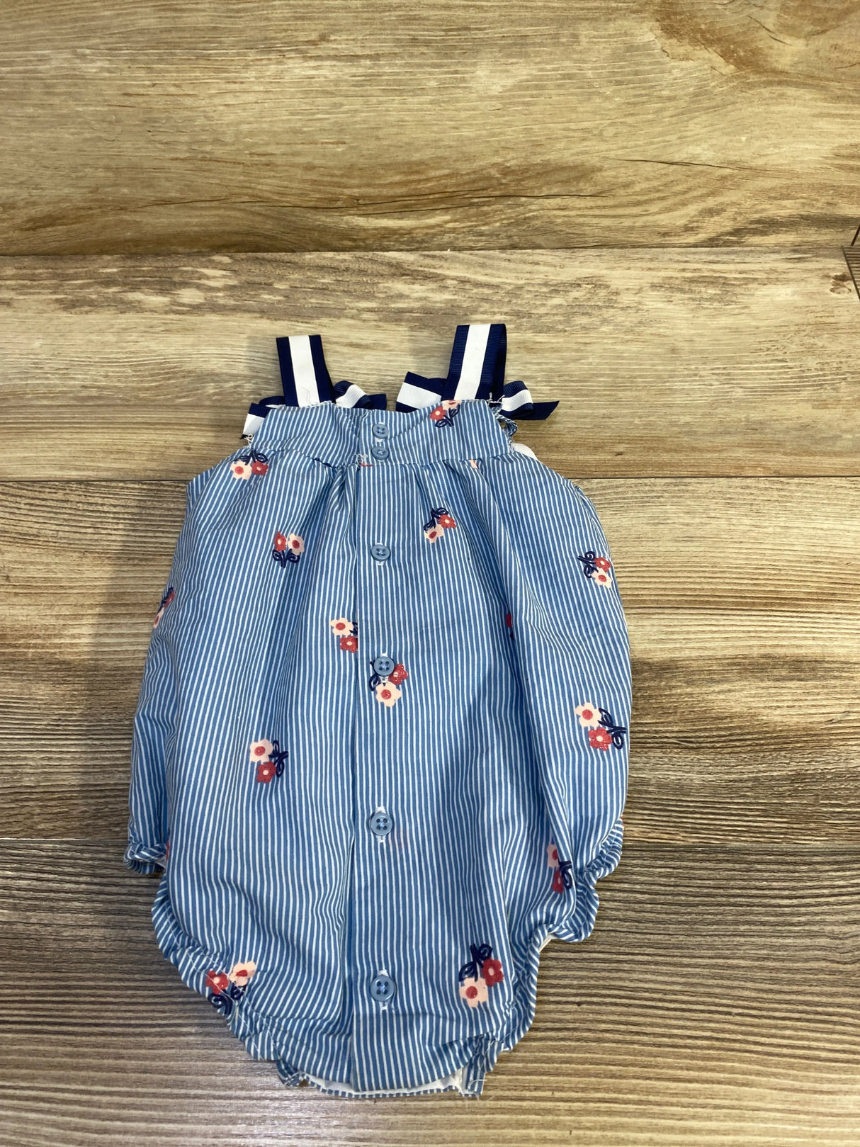 Front view of light blue Baby Starters romper with pinstripes, small floral print, navy bow straps and front buttons