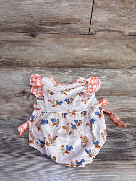 Flat lay of ivory baby bubble romper with rooster print, orange gingham ruffle sleeves and side ties on wood background
