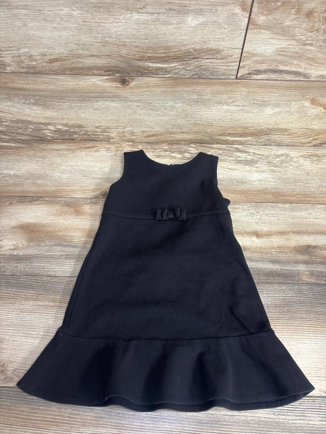 Gently used sleeveless black toddler dress with ruffled hem and small bow on waist, laid on wooden floor