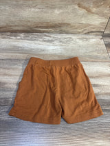 Flat lay of The 5th Legacy caramel brown toddler shorts (18-24 months) showing elastic waistband and straight hem on wood background