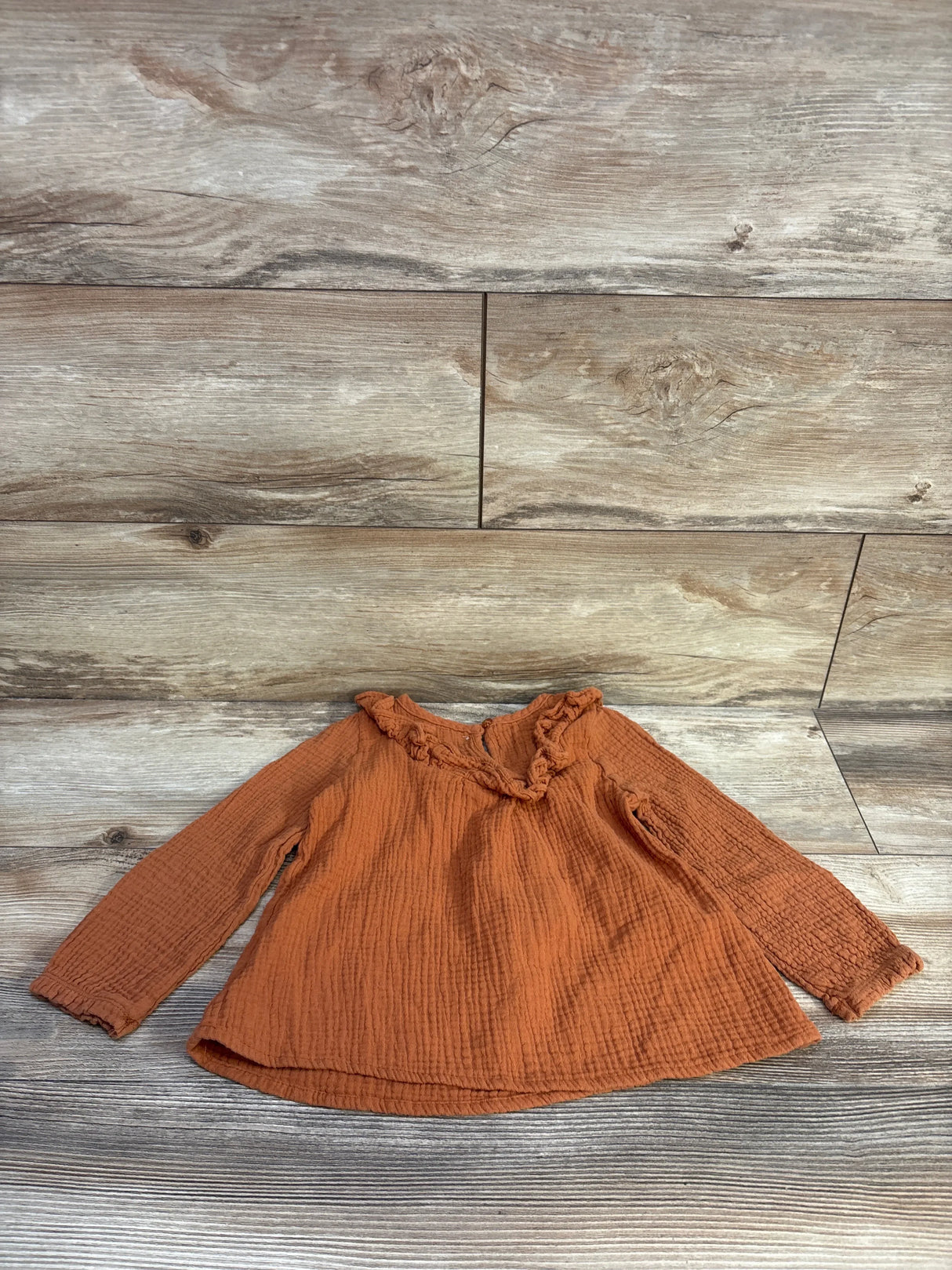 Flat lay of caramel Tahari gauze long-sleeve shirt 4T showing ruffled collar and smocked cuffs on wood background